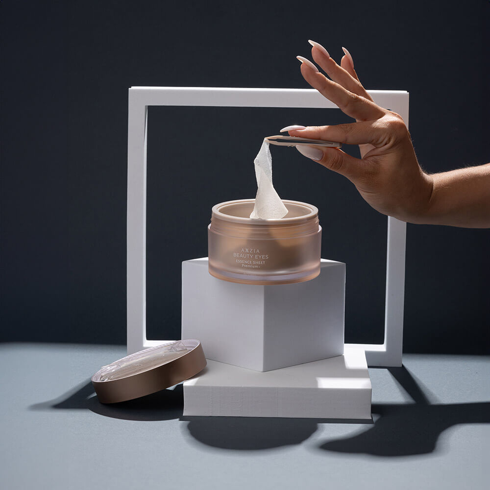 Инсталяция: женская рука достает пинцетом патчи AXXZIA BEAUTY EYES Essence Sheet Premium + из банки